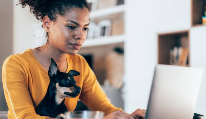 Mulher usando um notebook enquanto o cachorro está sentado em seu colo