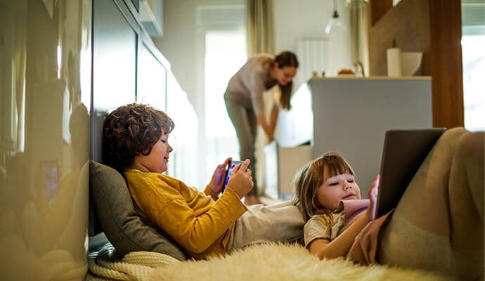 Crianças usando tablets enquanto a mãe está em segundo plano