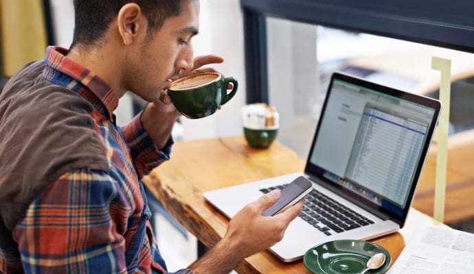 Homem tomando café enquanto olha para o celular.