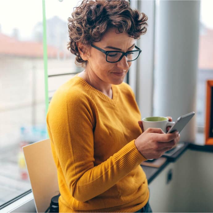 Mulher segurando uma xícara e um telefone celular