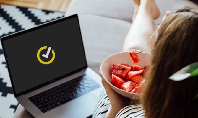 Mulher comendo frutas ao lado de um laptop aberto