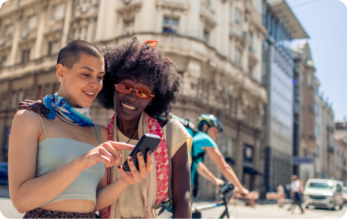 Duas mulheres sorrindo e olhando um celular juntas
